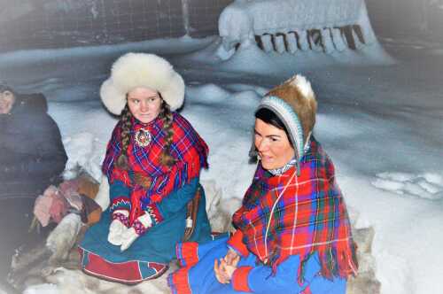 Woman and girl dressed in Sami clothing sitting in the snow.