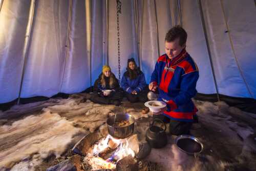 Mann kledd i samisk kofte serverer mat i lavvo