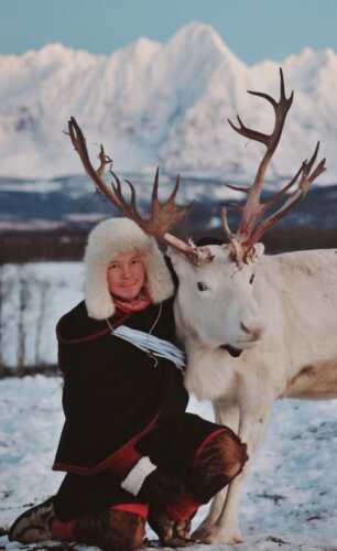 Mann som holder hvitt reinsdyr i vinterlandskap.