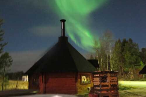 Northern lights across the sky behind a small hut