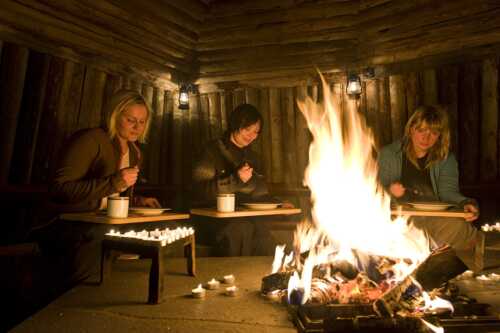 3 damer sitter rundt bålet inne i lavvo og spiser.